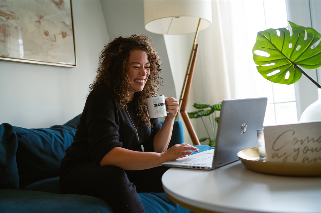 Dina Scippa laughing while working on a laptop with a coffee mug