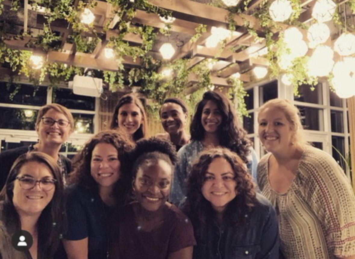 A group of women smiling together under string lights at an outdoor gathering