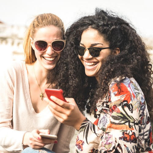 Two women are smiling and looking at a cell phone.