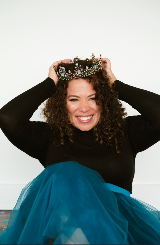 A woman wearing a tiara and holding her head.